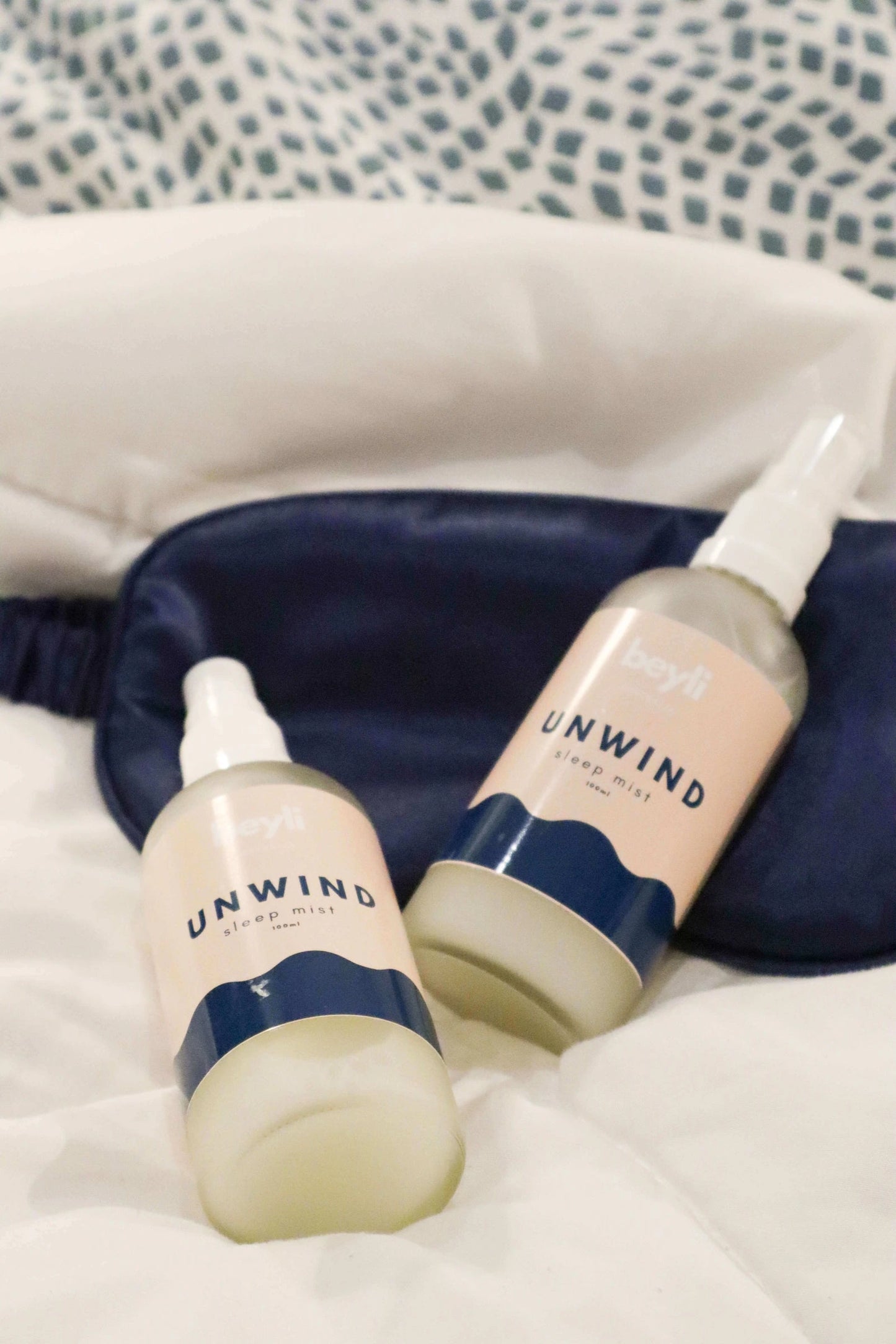 A set of sleep aid products with a mist bottle on a cozy bed setting