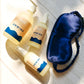 A set including a blue sleep eye mask, body wash, and hand sanitizer arranged on a bathroom counter