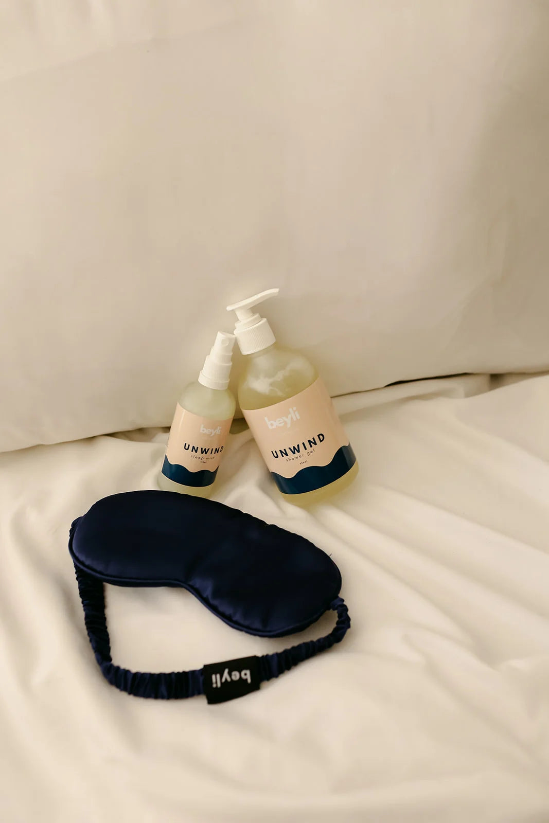 A memory foam sleep eye mask with a bottle of hand sanitizer on a soft bedspread